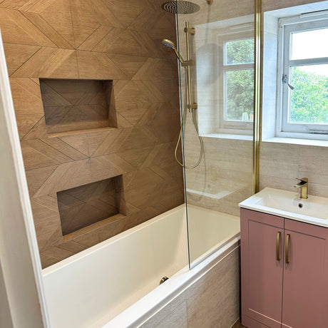 Bathroom with wood-effect tiled feature wall, recessed shower niches, brushed brass fittings, and a pink vanity unit