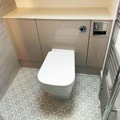 Toilet built into fitted storage beneath a sloped ceiling, with a chrome heated towel rail and the same patterned floor tile underfoot.